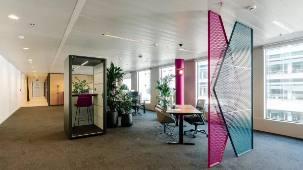 Modern kantoor met een kleurrijke roomdivider, een zwarte belcel en planten bij de werkplekken en bureaus.